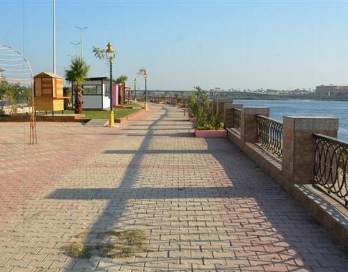 A serene riverside walkway with brick pavement, ornate metal railings, and lamp posts against a clear blue sky