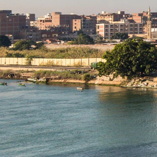 View of a bustling cityscape by the river with buildings in the background and boats on the water