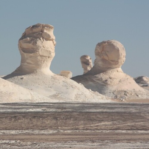 Two large, naturally sculpted rock formations resembling giant heads overlooking a barren desert landscape
