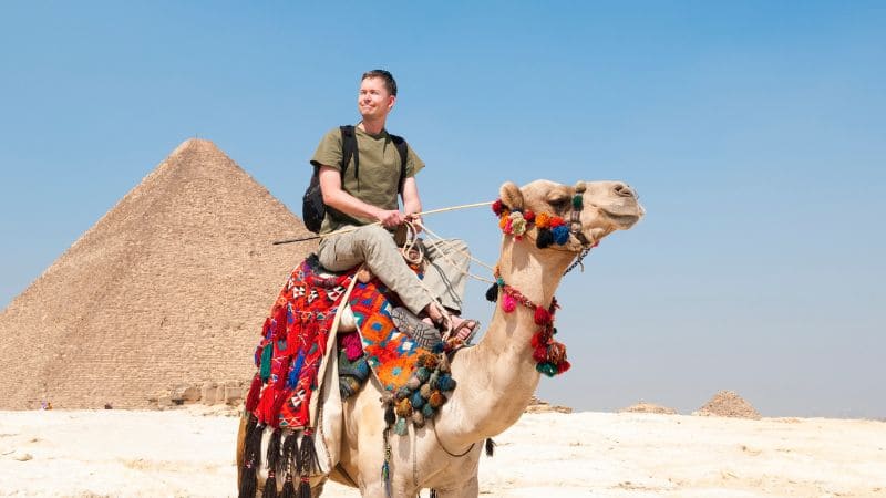 A traveler standing in front of a beautifully preserved ancient Egyptian temple, surrounded by carved walls and columns