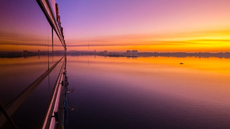 Sunset reflecting on calm waters viewed from a glass structure.