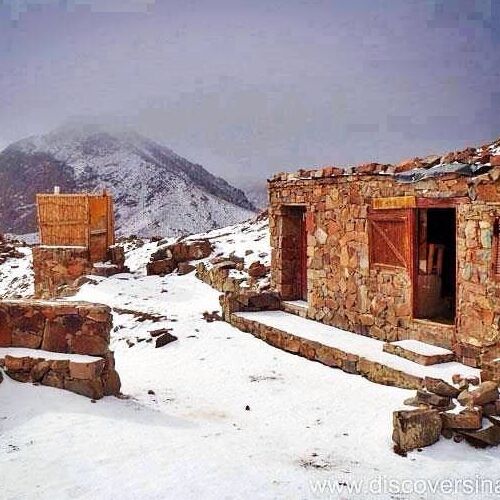 Snow-covered stone cabins on a mountain slope with misty peaks in the background