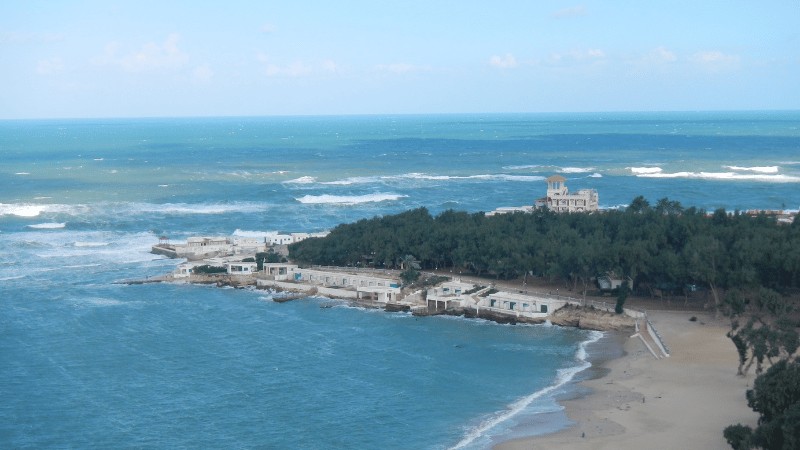 "A panoramic view of a Mediterranean coastline with a historic building overlooking the sea."