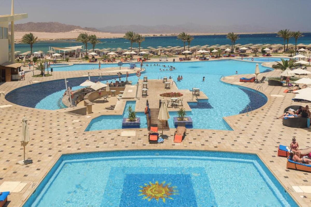 A panoramic view of the Barceló Tiran Sharm Resort featuring the pool area and beachfront, with lush palm trees and clear blue skies