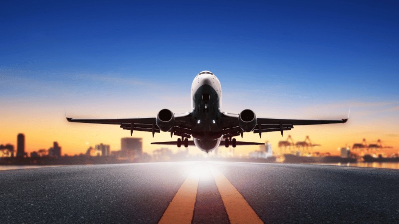 "Commercial airplane taking off from a runway at dawn with the city skyline in the background."