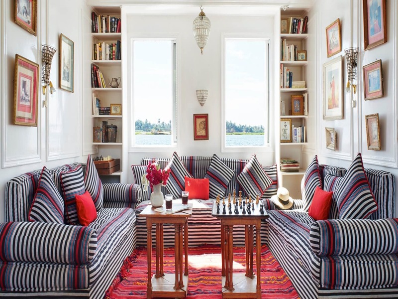 Cozy lounge area with striped sofas, colorful cushions, and large windows offering views of the Nile River