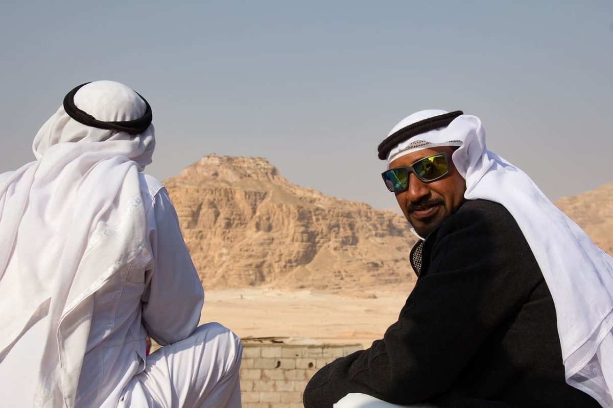A group of Egyptian Bedouin men in traditional attire, gathered in a desert setting, sharing a moment of community and culture.