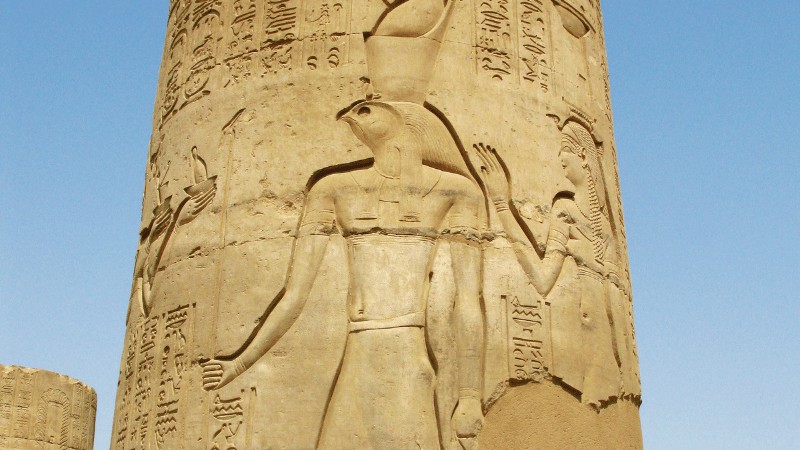 "Relief of a traditional Egyptian deity with a falcon head and a female figure, both carved in hieroglyphic-covered stone."