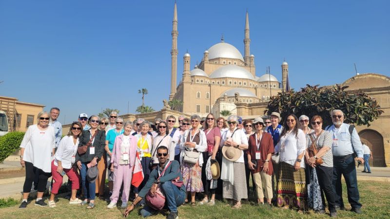 A group of tourists standing on a grassy area in front of the majestic Mosque of Muhammad Ali in Cairo, Egypt