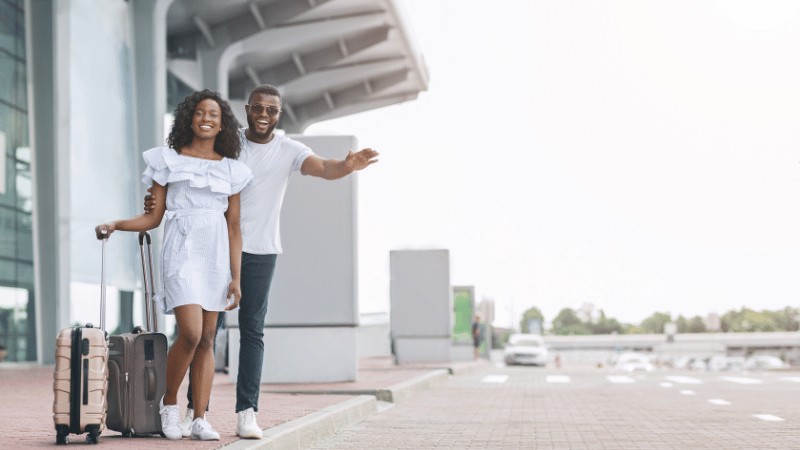 "A cheerful couple with luggage hailing a taxi outside the airport."