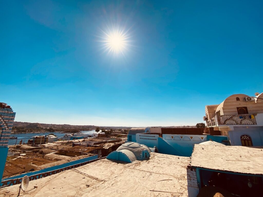 Blue and white Nubian rooftops under a bright sun with the Nile River in the distance.