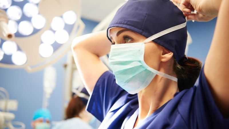 A surgeon adjusting her mask and preparing for surgery in a brightly lit operating room