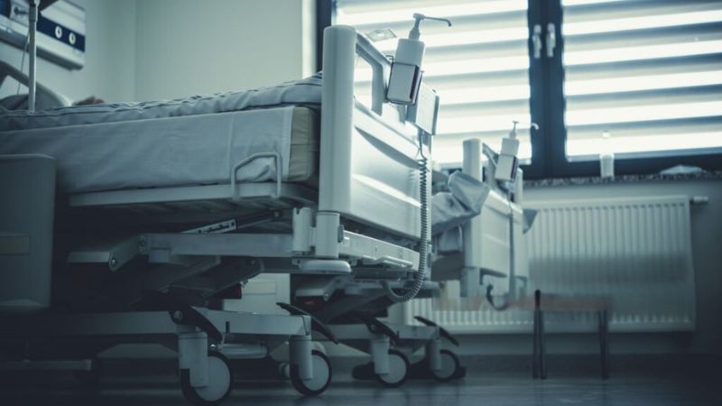Rows of empty hospital beds in a clean and well-lit ward with large windows
