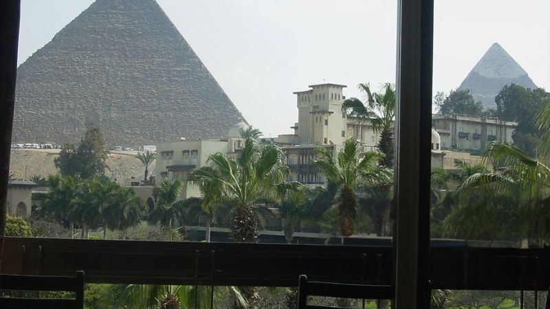 Close-up view of the Pyramids of Giza framed by palm trees and a building