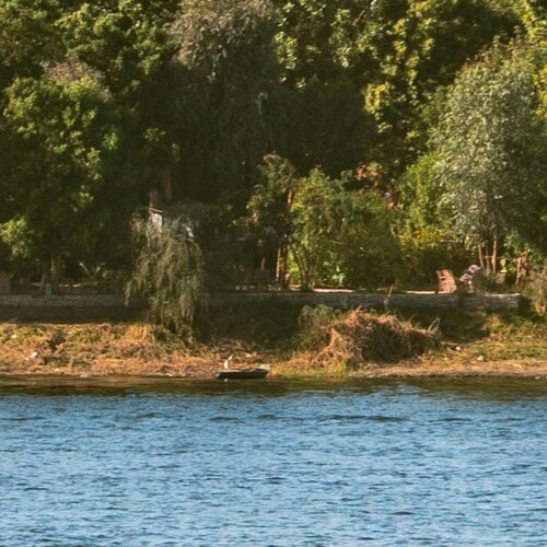 A serene river with lush greenery on the bank and a small boat moored near the shore