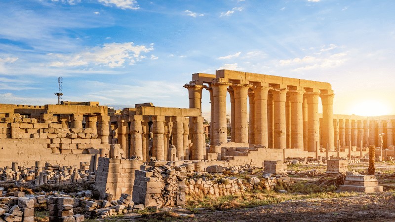 "Sunrise behind the towering columns of an ancient temple ruin."