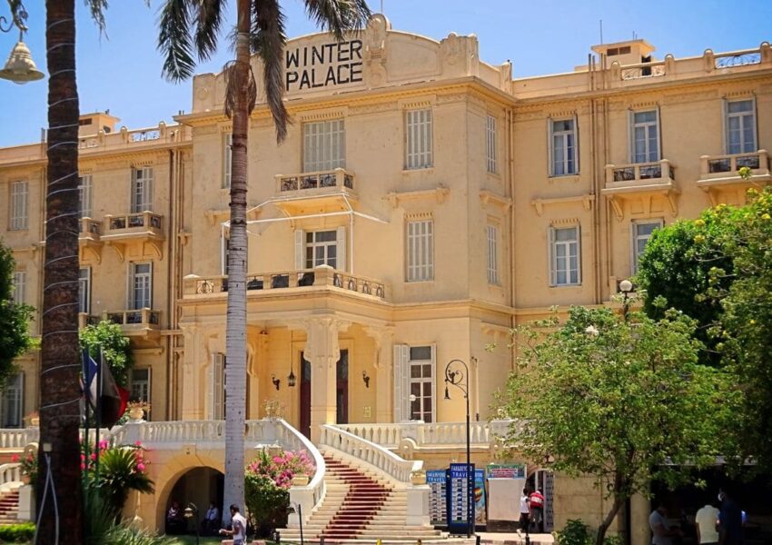 Front view of the historic Winter Palace Hotel in Luxor, Egypt, surrounded by lush greenery under a clear blue sky