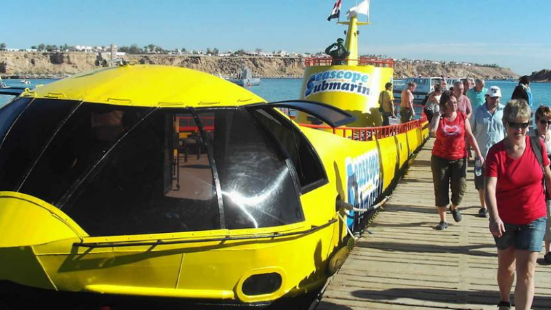 Tourists walking towards a yellow seascope submarine on a pier.