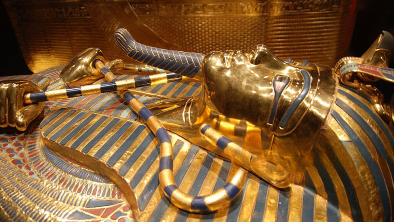 The golden mask of Tutankhamun, adorned with blue and gold stripes, displayed in a museum.